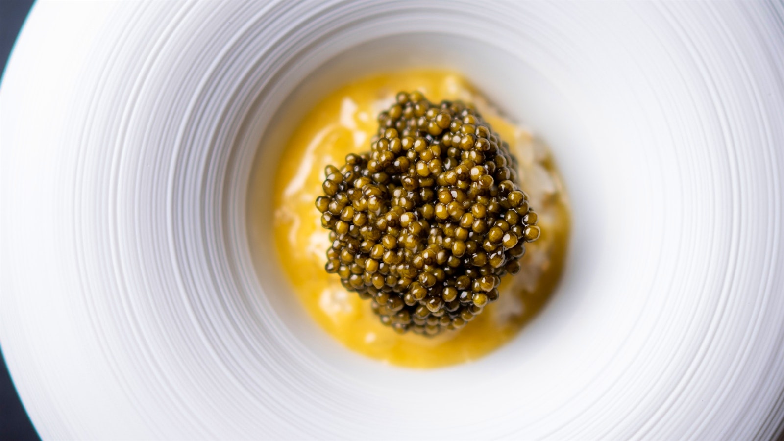 A white dish of sesame-flavored Koshihikari rice served over a silky smoked sabayon and topped with Regiis Ova caviar